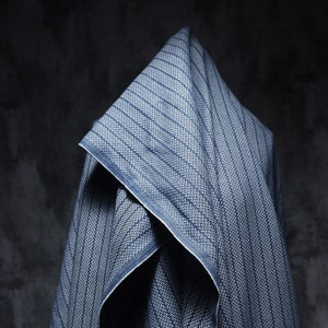 May include: A blue and white striped fabric with a herringbone pattern. The fabric is folded and draped over a surface.
