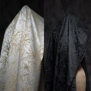 May include: Two fabric samples with a bamboo pattern. One sample is white with a gold bamboo pattern, the other is black with a black bamboo pattern.