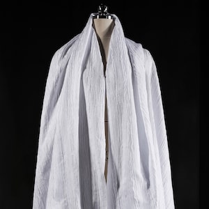 May include: White, textured fabric draped over a dress form. The fabric is gathered and folded, creating a flowing and dramatic look.