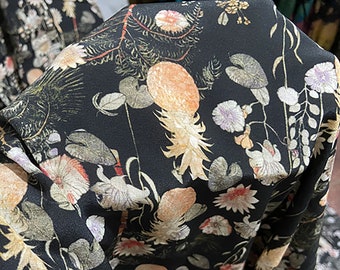 May include: Black fabric with a floral print featuring a variety of flowers, leaves, and pineapples. The fabric has a subtle sheen and a soft texture.