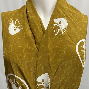 May include: A mustard yellow fabric with a white silhouette of a shrimp repeated throughout the fabric. The fabric has a textured, almost cracked, appearance. A green ribbon is tied around the fabric.