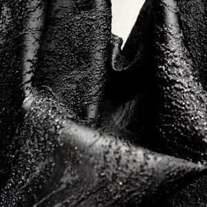 Peut inclure: Tissu noir avec une surface texturée et bosselée. Le tissu est plié et drapé, créant une composition dramatique et abstraite.