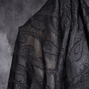 Puede incluir: Tela negra transparente con un patrón de plumas de pavo real en relieve.