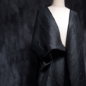 May include: Black fabric with a textured pattern of circles. The fabric is draped over a dress form.