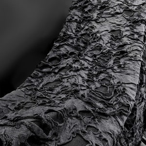 May include: A black fabric with a distressed, ripped, and torn texture. The fabric has a pattern of holes and tears throughout.