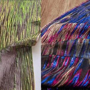 Peut inclure: Deux échantillons de tissu avec une finition texturée et irisée. L'un est principalement vert et marron, l'autre présente des rayures bleues, roses et dorées. Le tissu est plié, mettant en valeur sa texture et ses variations de couleurs.