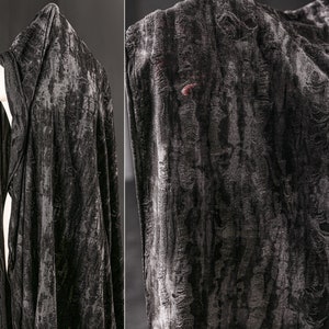 Peut inclure: Une cape à capuche en velours noir avec un aspect texturé et vieilli. Le tissu a un léger brillant et un motif légèrement en relief.