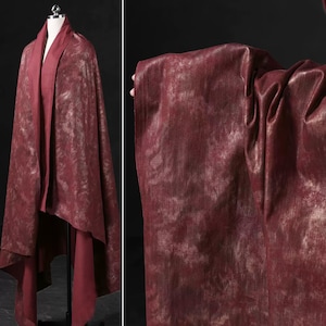 May include: A burgundy fabric with a subtle gold shimmer. The fabric has a textured, almost marbled appearance.