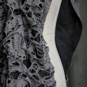 May include: Gray fabric with a distressed, ripped, and torn design. The fabric has a lace-like appearance with many holes and tears.