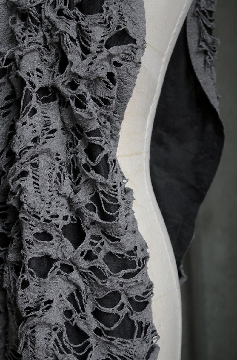 May include: Gray fabric with a distressed, ripped, and torn design. The fabric has a lace-like appearance with many holes and tears.