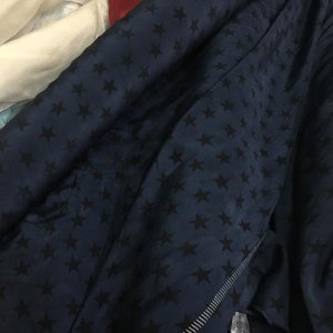 Pode incluir: Um tecido azul escuro com um padrão de estrelas pretas. O tecido está dobrado e tem um detalhe de zíper.
