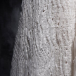May include: White fabric with a textured, wavy pattern. The fabric is soft and delicate, with a slightly sheer appearance.