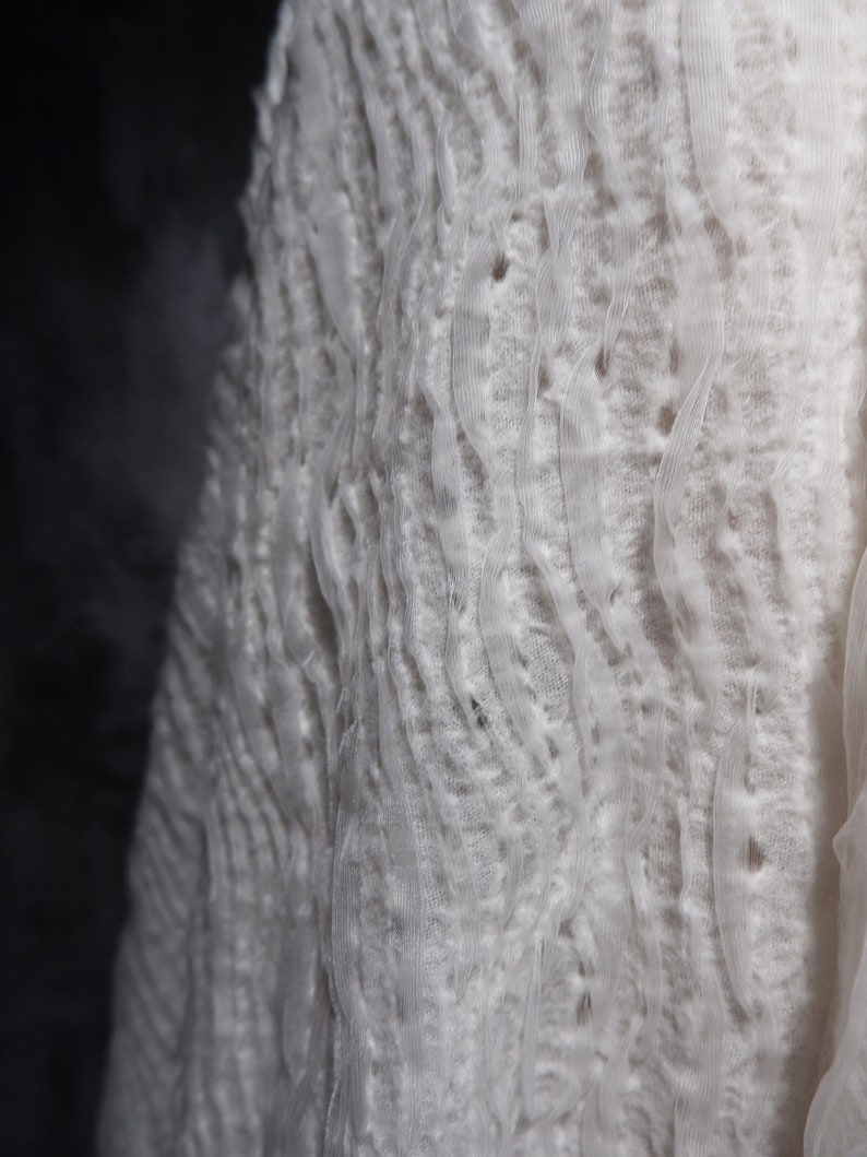 May include: White fabric with a textured, wavy pattern. The fabric is soft and delicate, with a slightly sheer appearance.