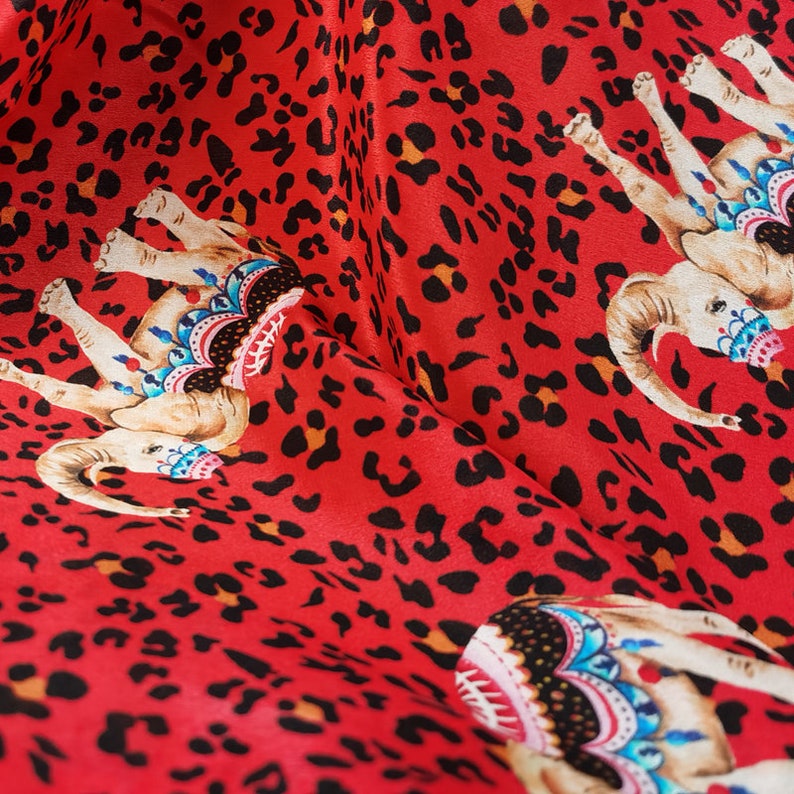 May include: Red fabric with a leopard print pattern featuring colorful elephants with intricate designs. The fabric is soft and silky.