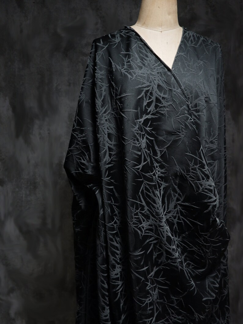 May include: Black fabric with a subtle embossed pattern of branches. The fabric has a silky sheen and a soft drape.