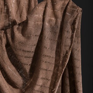 May include: A brown knitted fabric with a textured pattern. The fabric is folded and draped over itself.