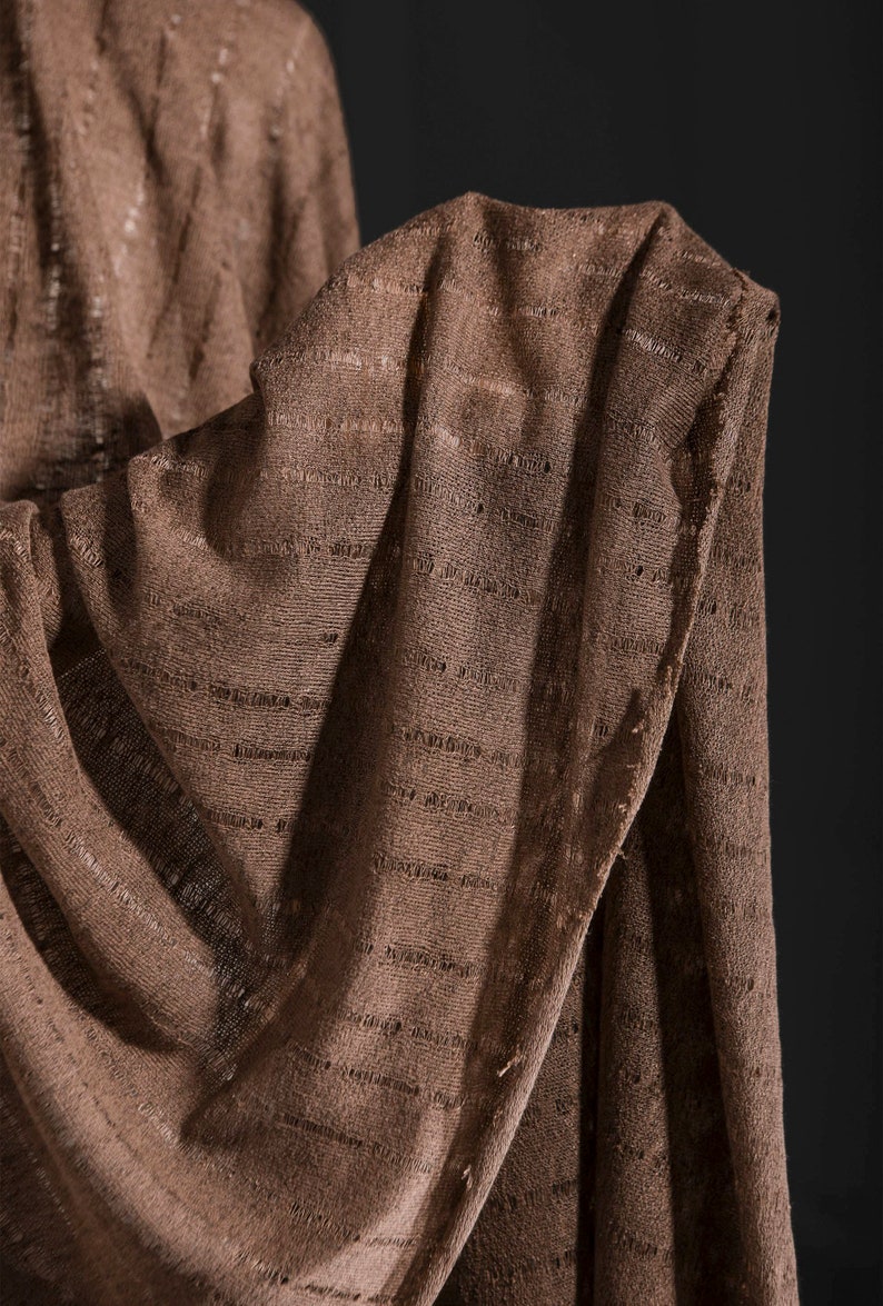 May include: A brown knitted fabric with a textured pattern. The fabric is folded and draped over itself.