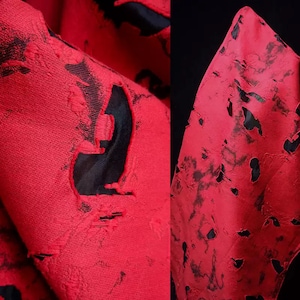 Puede incluir: Tela roja con parches negros desgastados. La tela tiene una superficie texturizada.