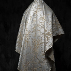 May include: A white fabric with a gold bamboo pattern draped over a dark background.