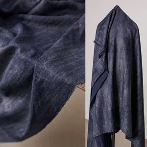 May include: Close-up of a dark blue fabric with a textured, slightly faded appearance. The fabric is draped and folded, revealing its texture and the raw edge of the material. The fabric is likely used for clothing or home decor.