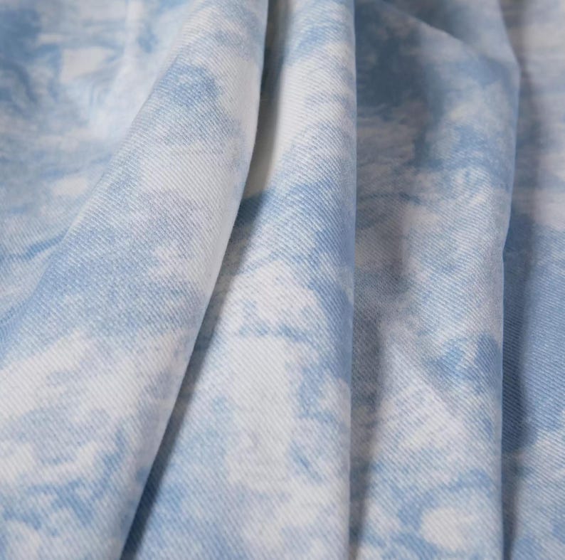 Op de afbeelding: Close-up van een lichtblauwe stof met een wit tie-dye patroon. De stof is zacht en heeft een subtiele textuur.