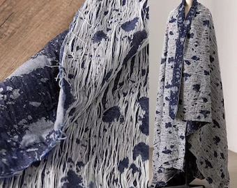 May include: A gray and navy blue textile with a unique, distressed design. The fabric features a pattern of dark blue splatters and vertical, frayed lines. The textile is draped over a mannequin, showcasing its full length and texture.