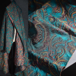 Könnte beinhalten: Türkisfarbener Stoff mit einem Paisley-Muster in Gold-, Burgunder- und Türkistönen. Der Stoff ist drapiert, wodurch seine Textur und sein Muster hervorgehoben werden. Die Nahaufnahme zeigt die komplizierten Details des Musters.