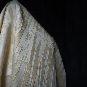 May include: Close-up of a white fabric with a textured, embossed pattern of beige stripes. The fabric has a soft, luxurious feel.