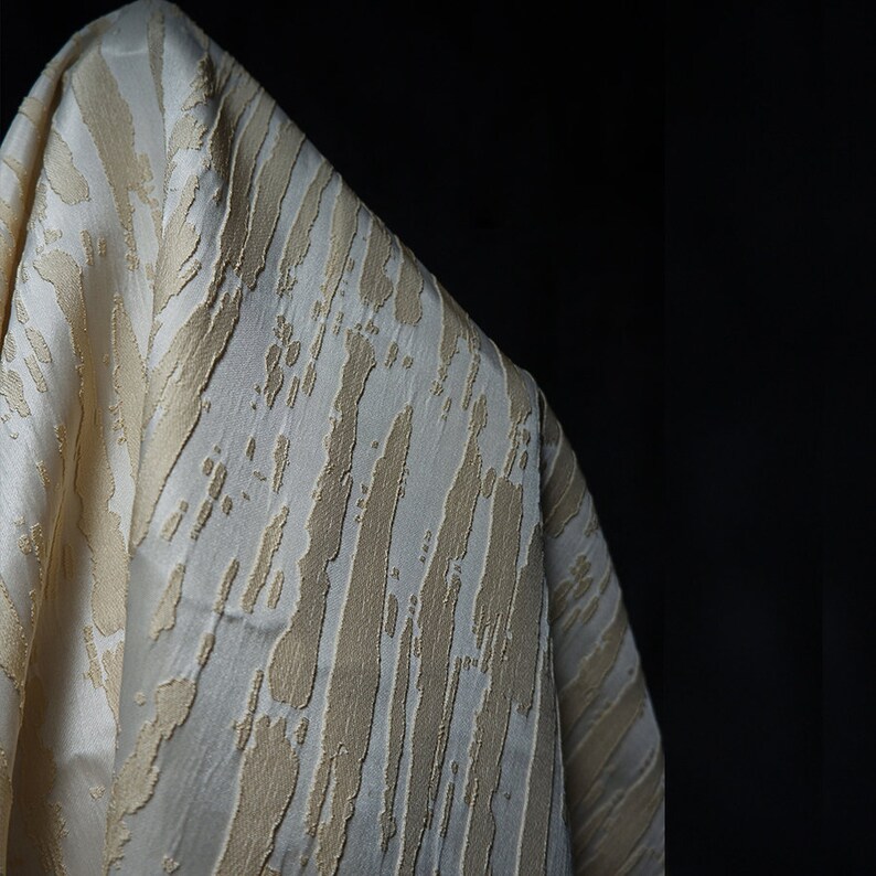 May include: Close-up of a white fabric with a textured, embossed pattern of beige stripes. The fabric has a soft, luxurious feel.