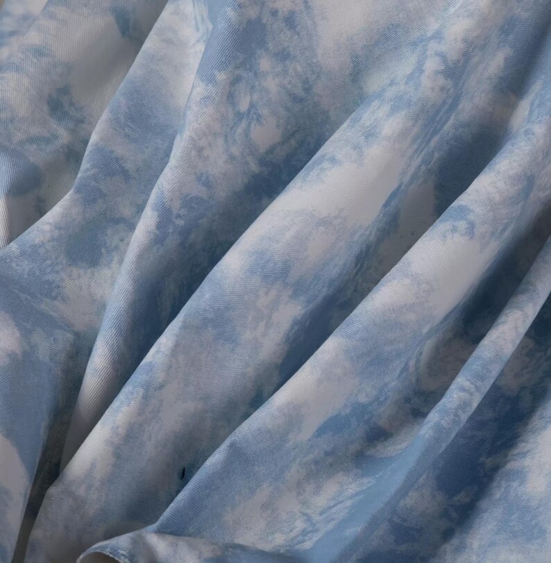 Op de afbeelding: Close-up van een blauwe en witte tie-dye stof. De stof heeft een zachte, vloeiende textuur en een subtiele, vervaagde uitstraling.