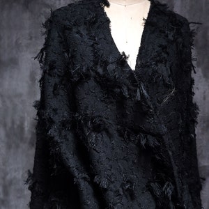 May include: Black fabric with a textured, fuzzy surface. The fabric has a v-neck and is draped over a mannequin.