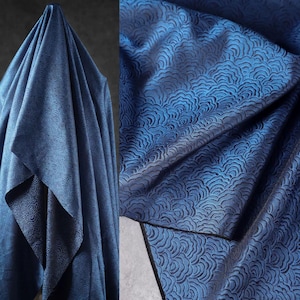 May include: A close-up of a draped, textured fabric in shades of blue. The fabric has a repeating wave-like pattern. The folds and shadows create depth and dimension, highlighting the intricate design. The fabric appears to be a luxurious material.