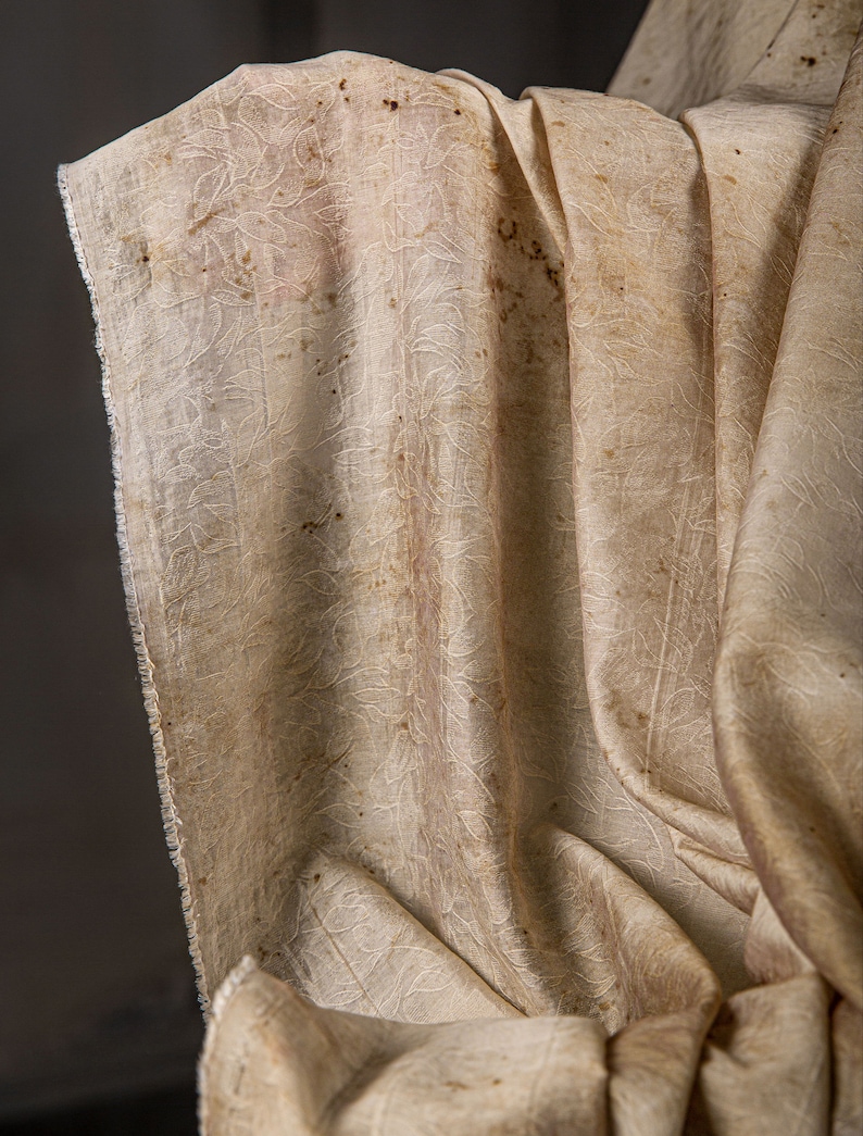 May include: A close-up of a beige fabric with a textured pattern and brown stains.