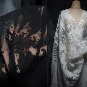 Op de afbeelding: Witte, doorschijnende stof met een zwart-wit abstract patroon. De stof is gedrapeerd over een mannequin.