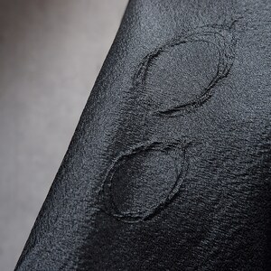 May include: A close-up of a black fabric with a stitched design of two overlapping circles.