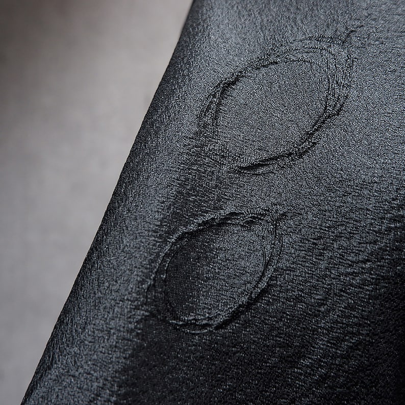 May include: A close-up of a black fabric with a stitched design of two overlapping circles.