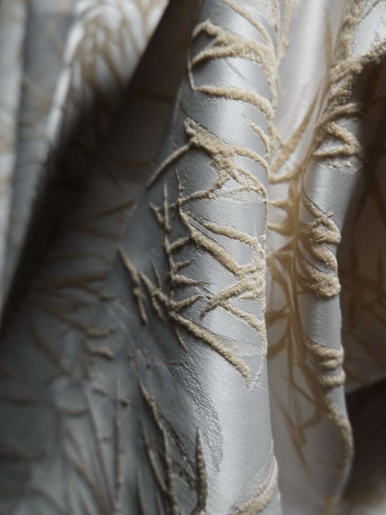 May include: Close-up of a silver fabric with a raised, textured pattern of beige lines and swirls.