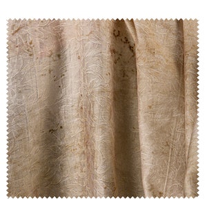 May include: A close-up of a beige fabric with a subtle floral pattern. The fabric has brown stains and appears to be old and worn.