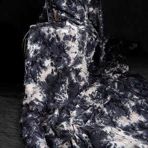May include: A dark fabric with a tie-dye pattern in shades of black and white. The fabric is draped over a chair, with the edges frayed, creating a textured and layered effect. The overall aesthetic is modern and artistic.