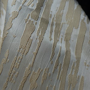 May include: White fabric with a textured pattern of gold stripes. The stripes are uneven and have a brushstroke effect.