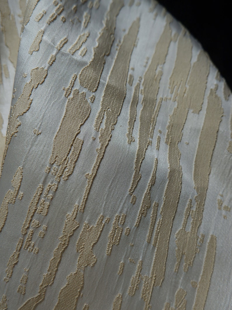 May include: White fabric with a textured pattern of gold stripes. The stripes are uneven and have a brushstroke effect.