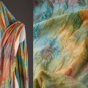 May include: A colourful tie-dye scarf with a fringed edge. The scarf is made of a soft, lightweight fabric and features a blend of blue, green, orange, and yellow hues.