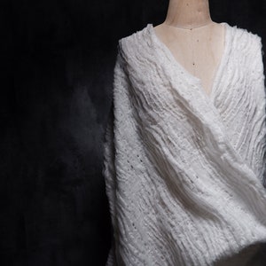 May include: A white, textured, crocheted shawl draped over a mannequin. The shawl has a loose, flowing design and is made of a soft, lightweight fabric.