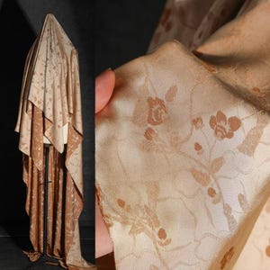Op de afbeelding: Een gedrapeerde stof met een bloemenpatroon in beige en bruine tinten. De stof wordt op een mannequin getoond, waarbij de drape en textuur worden benadrukt. Een close-up toont het ingewikkelde bloemendesign.