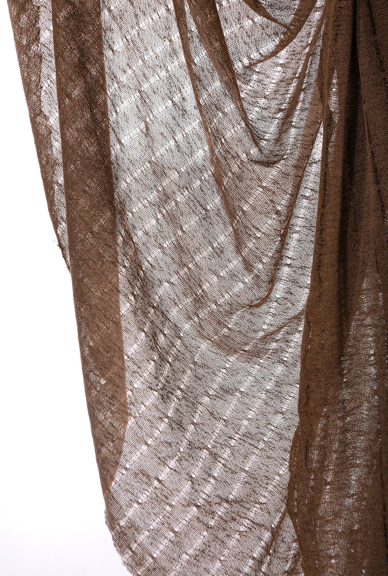 May include: A brown, sheer fabric with a woven pattern. The fabric is draped and folded, creating a textured look.