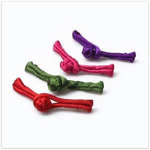 May include: Four fabric Chinese knot closures in red, green, purple, and pink. The knots are tied in a flower shape and are used to fasten garments.