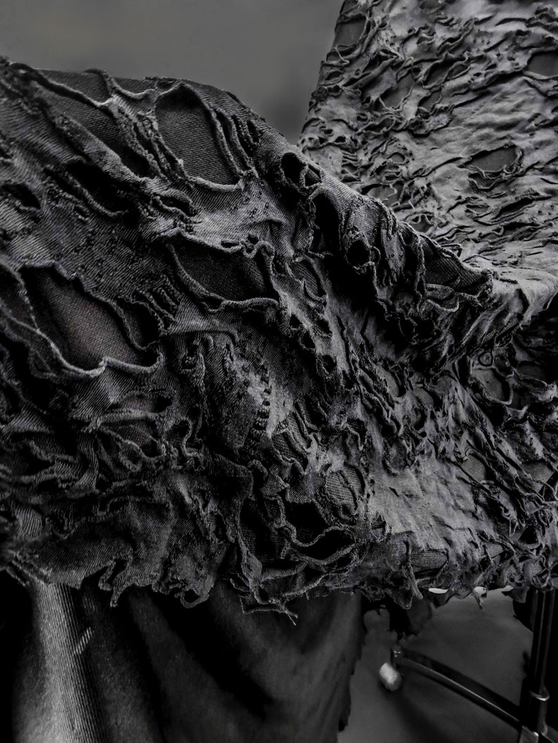 May include: Black fabric with a distressed, ripped, and frayed texture. The fabric is draped over a chair.