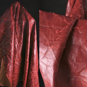 Peut inclure: Gros plan sur un tissu en cuir rouge avec une texture craquelée et vieillie. Le matériau est drapé et plié, révélant la profondeur et les détails de la surface. La couleur est un rouge profond et riche avec des veines rouges plus claires.