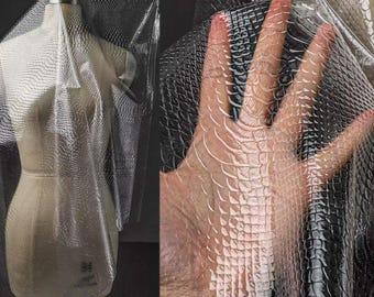 May include: A transparent, textured fabric with a reptile scale pattern is draped over a mannequin. The fabric is also held up by a hand, showing the texture and transparency. The fabric appears to be vinyl or a similar material.