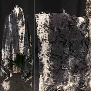 May include: A black and white frayed fabric shawl with a textured design. The fabric is soft and has a distressed look.